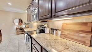 A modern kitchen with dark wood cabinets, granite countertops, and stainless steel appliances. - Uptown Aggie– 4BR Near Kyle Field (College Station)