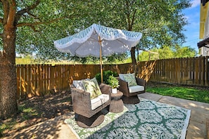 Une terrasse extérieure avec des meubles en osier, un parasol à rayures et un tapis décoratif.