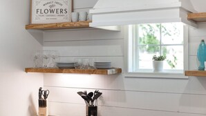 Una cocina con estantes de madera que exhiben utensilios de cocina y un letrero sobre flores frescas.