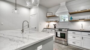 Una cocina moderna con armarios blancos, una isla de mármol, electrodomésticos de acero inoxidable e iluminación colgante.