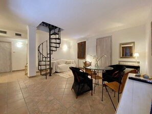 A spacious living area with a spiral staircase, a dining table with chairs, and a large mirror on the wall. - Appartamento di Charme con Vista Panoramica Sulla Campagna Toscana Fino al Mare (Guardistallo)