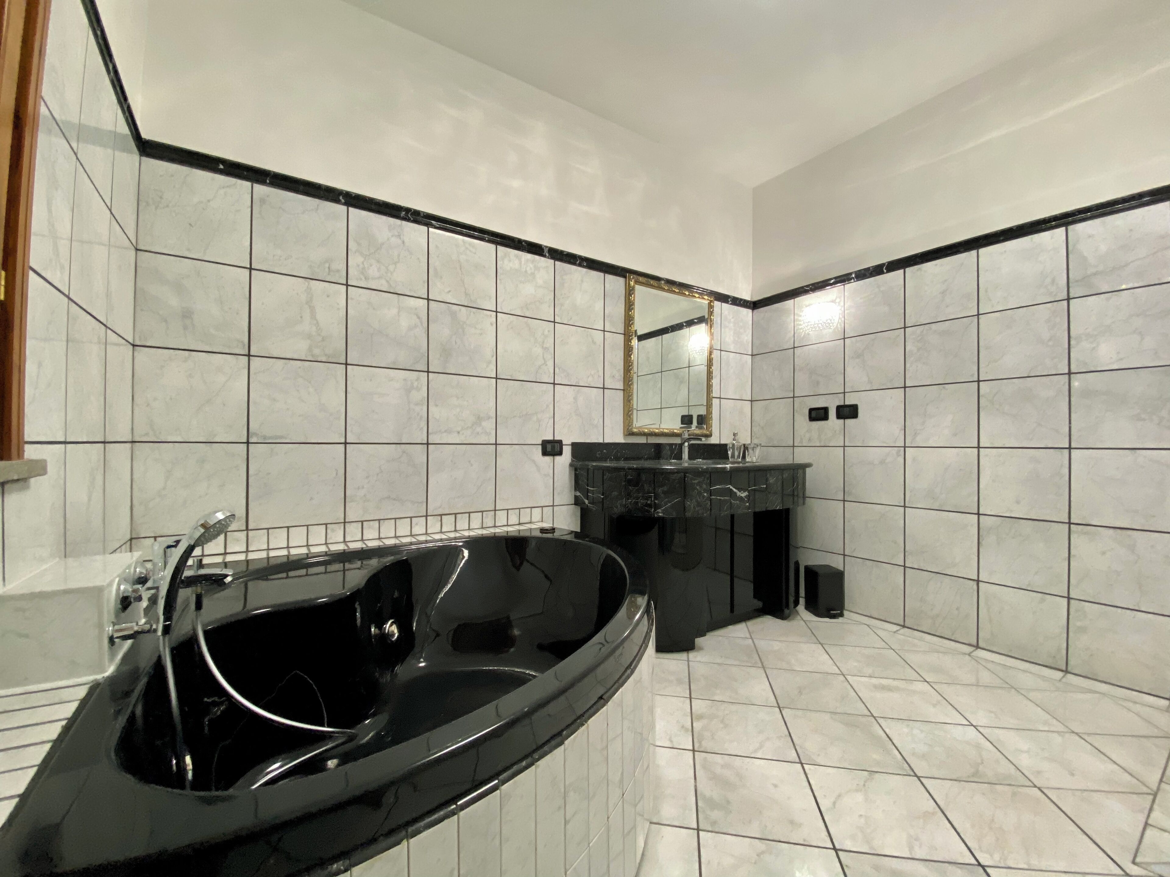 A modern bathroom with a black jacuzzi tub, a sink with a mirror, and tiled walls and floor.