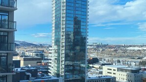 A tall glass building with a modern design, surrounded by other buildings and a parking lot. - Luxury 2 bedroom,  2 bath condo in the beautiful west end of downtown Calgary.  (Calgary)