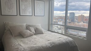 A bedroom with a large bed, a city view through a window, and three framed abstract artworks on the wall. - Luxury 2 bedroom,  2 bath condo in the beautiful west end of downtown Calgary.  (Calgary)
