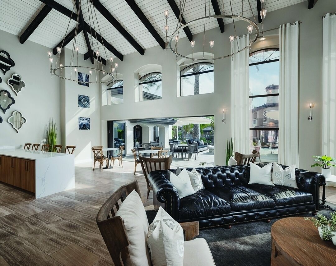 A spacious living area with a black leather sofa, wooden chairs, a coffee table, and a kitchen island.