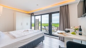 Habitación de hotel con cama, escritorio con una computadora portátil, botella de vino y vista a un campo verde por la ventana.
