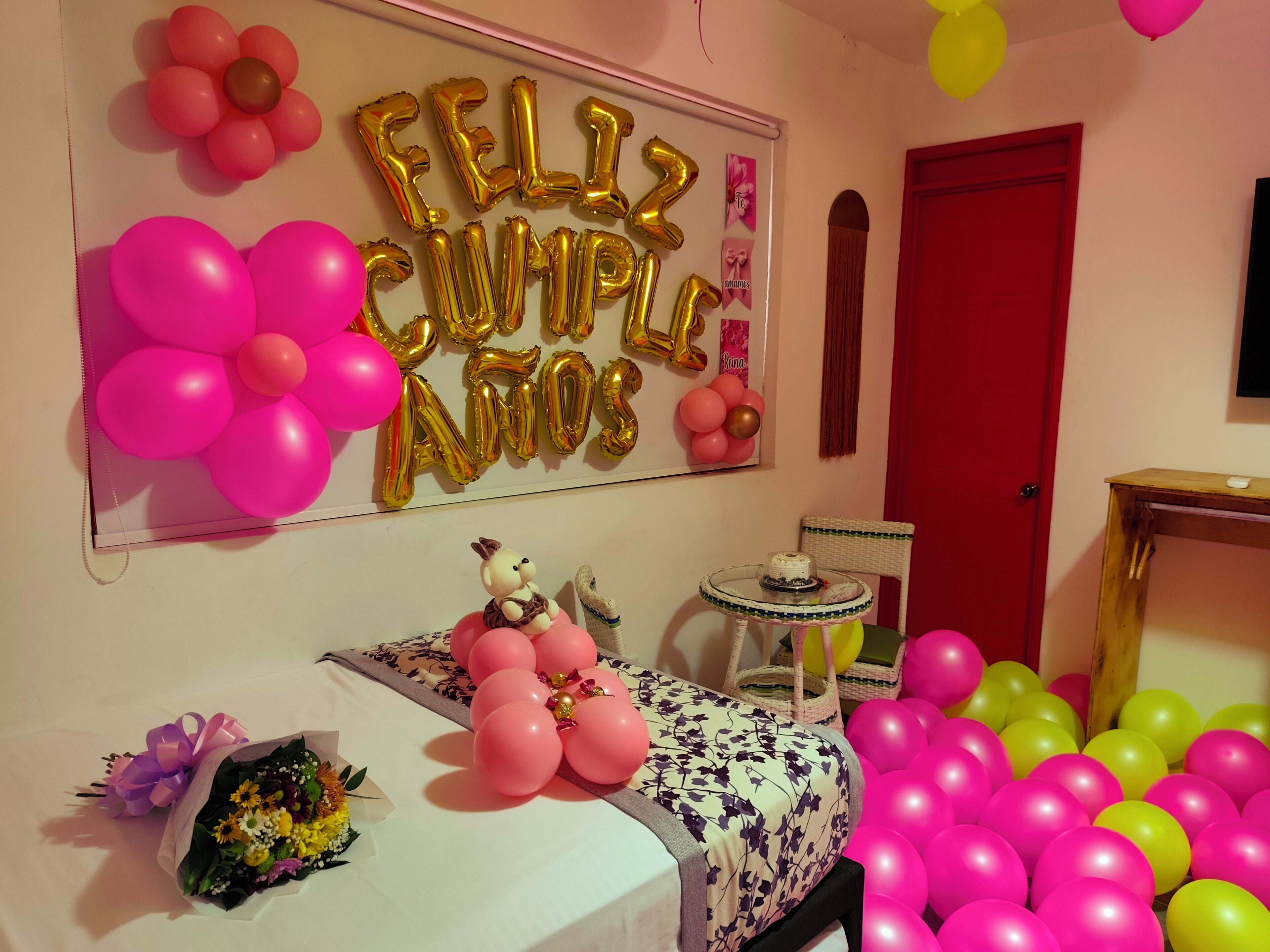 A room decorated for a birthday party with balloons, a cake, and a stuffed toy on the bed.