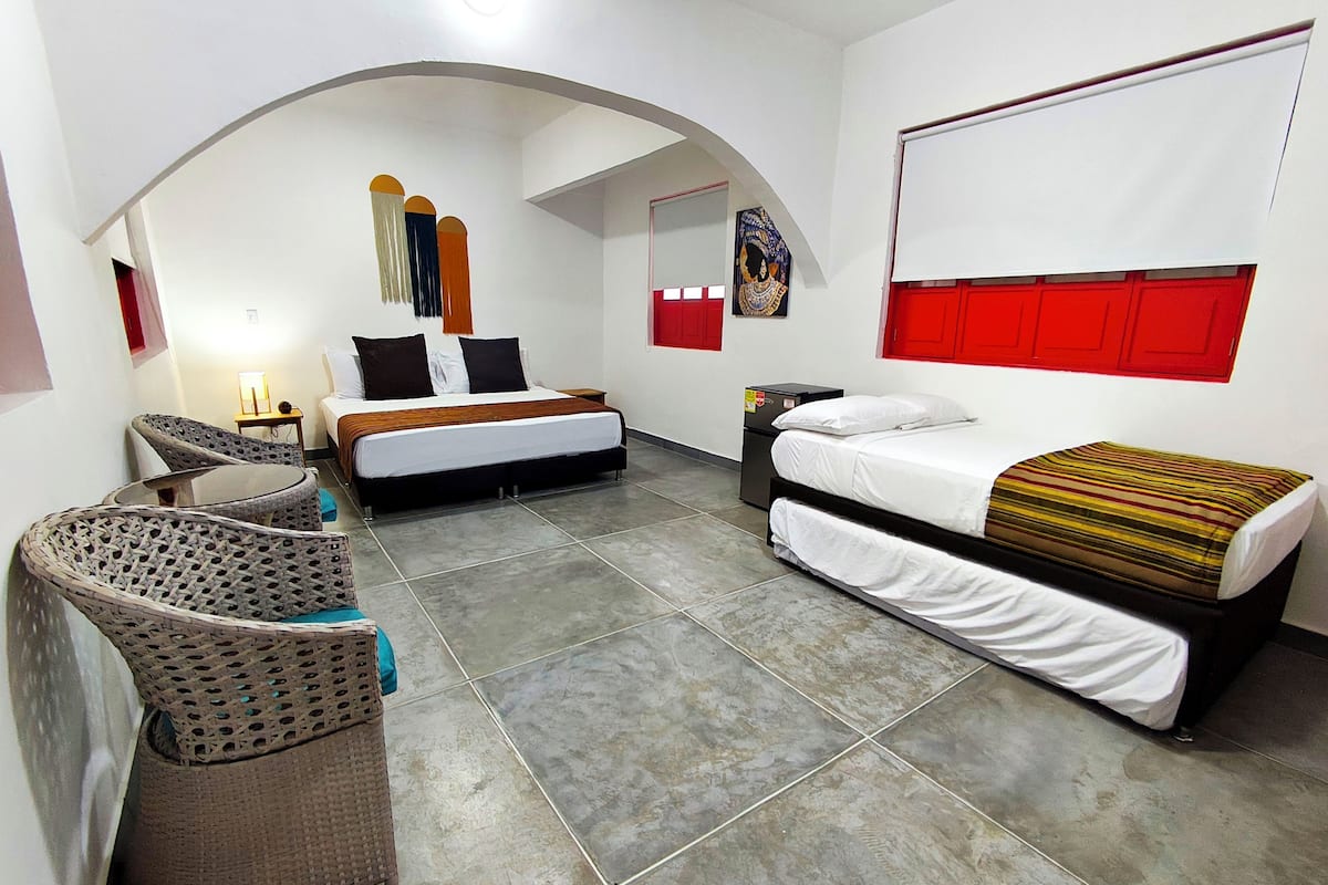 Ein Hotelzimmer mit einem Bett, einem zusätzlichen Bett, einem Sessel, einem Tisch und einer Wand mit einem roten Paneel.