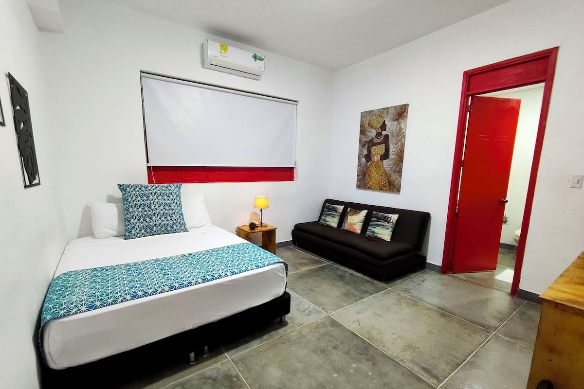 Ein Hotelzimmer mit Bett, Sofa, einer roten Tür und einer Wand-Klimaanlage.