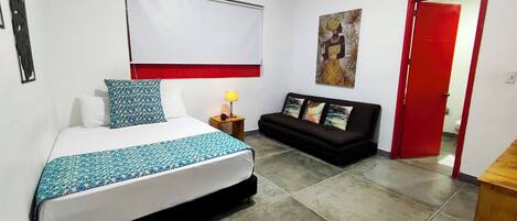 A hotel room with a bed, a sofa, a red door, and a wall-mounted air conditioner.