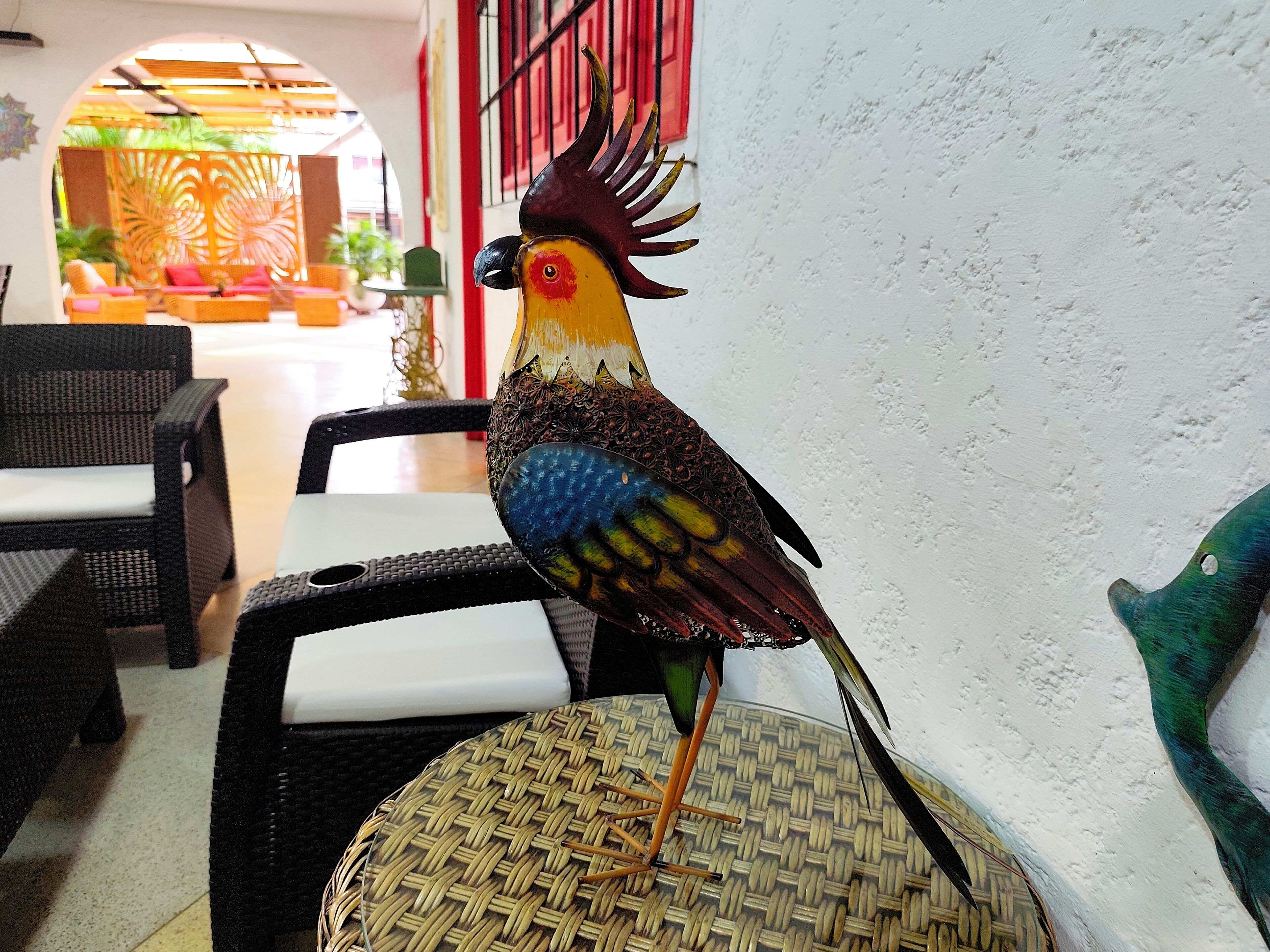 A bird sculpture on a wicker chair in a room with wicker furniture and a red door.