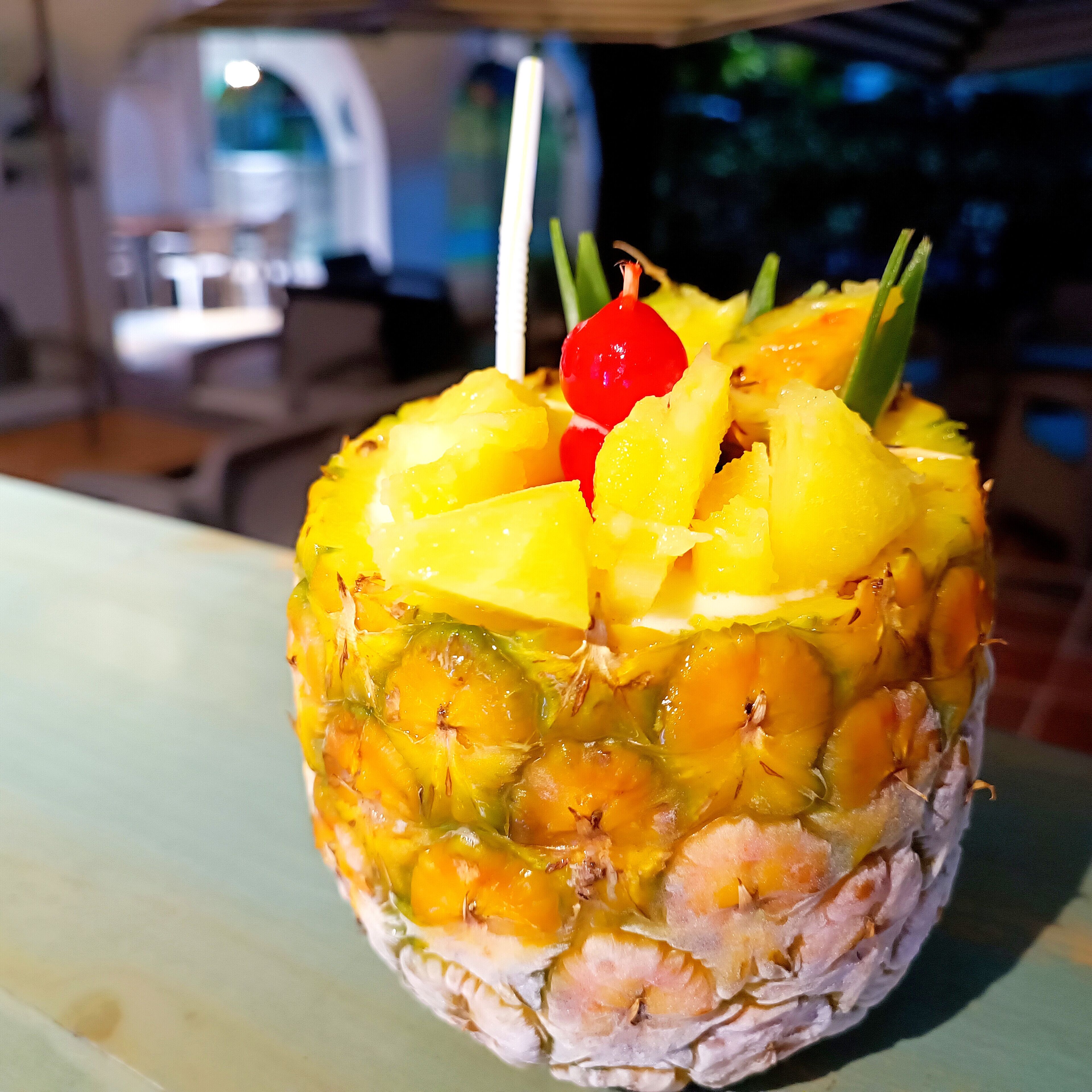 A pineapple with shrimp and pineapple chunks on top, garnished with a cherry and green leaves.