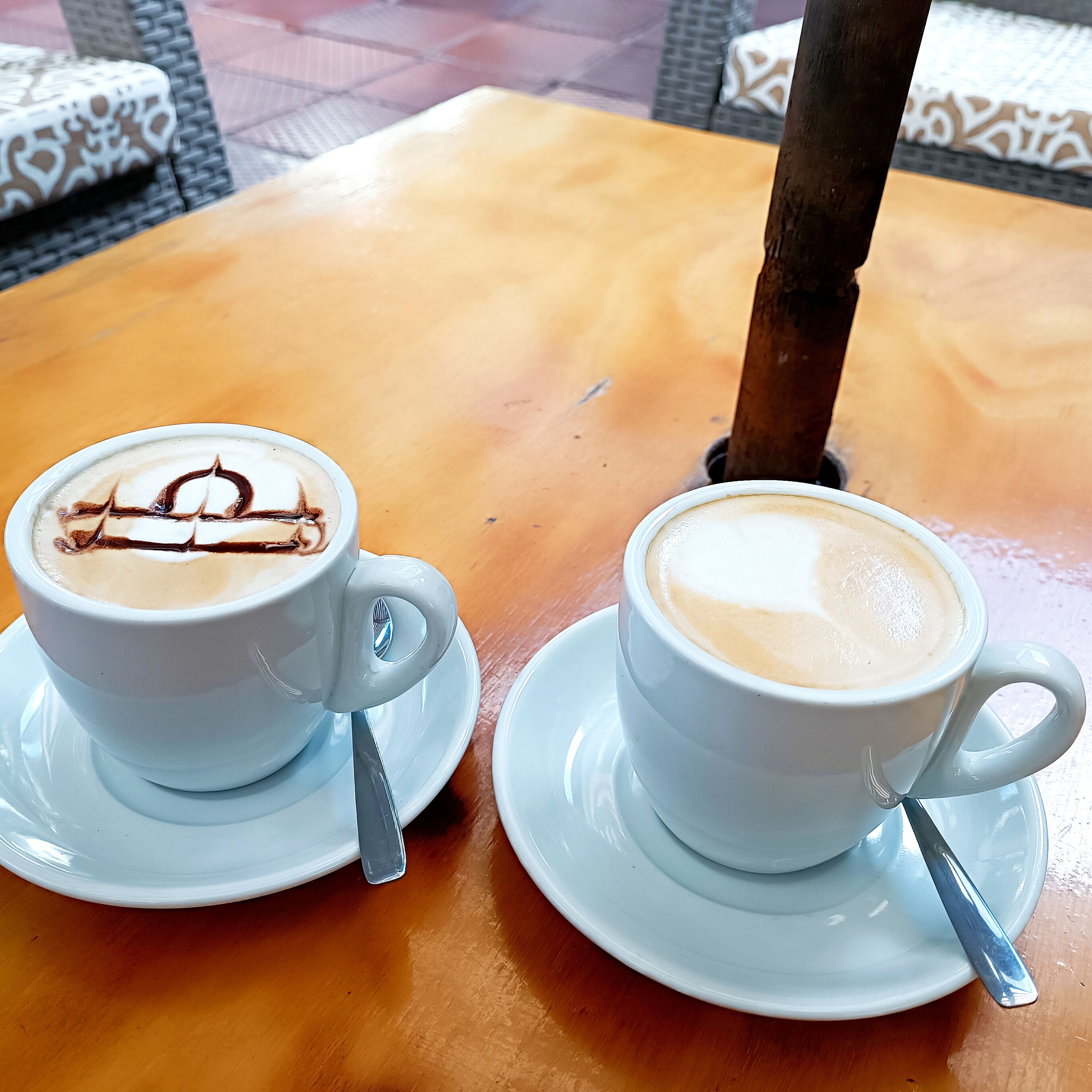 Dos tazas de café con leche y diseños de latte sobre una mesa de madera.