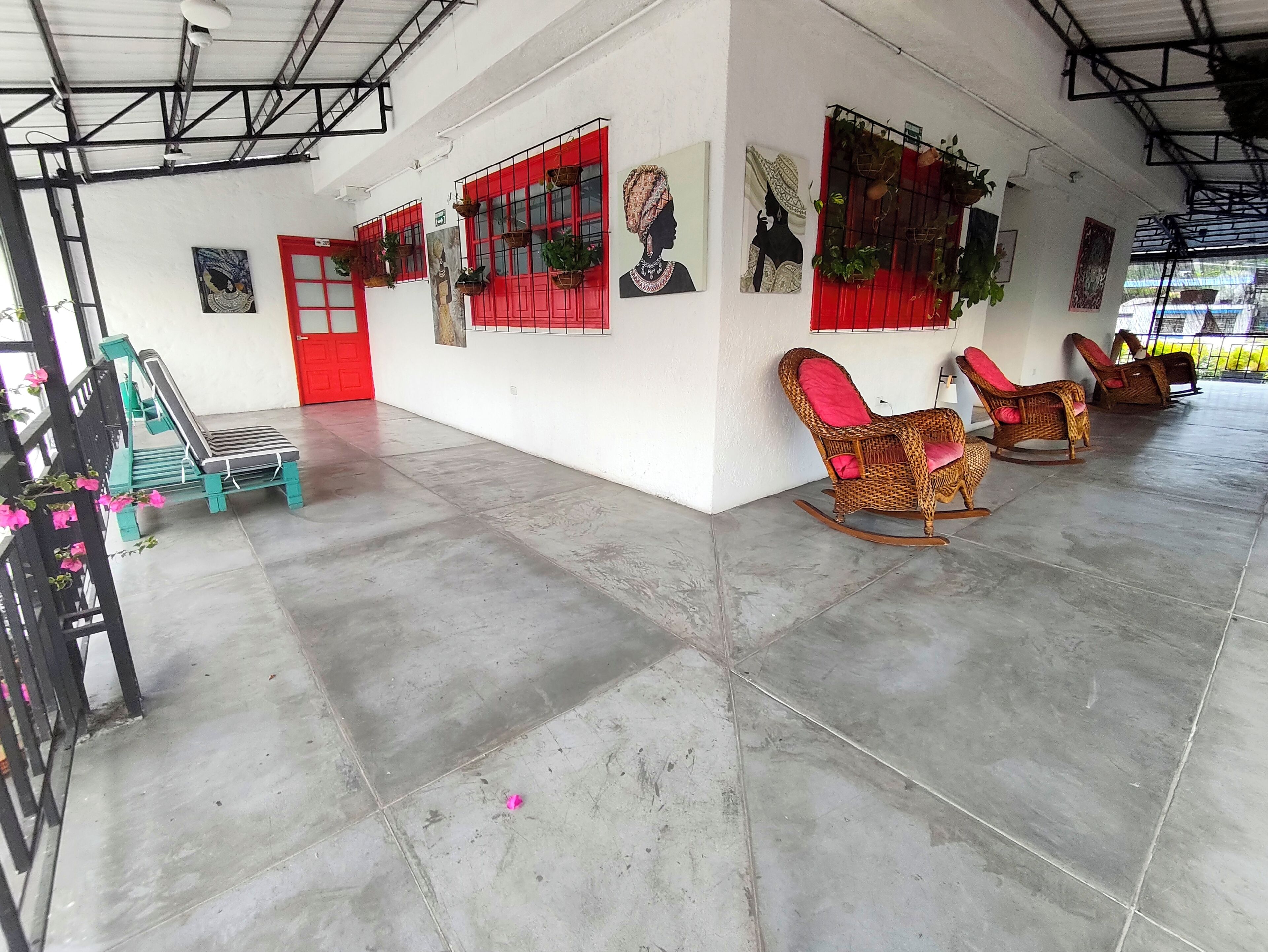 A spacious room with a high ceiling, red-framed windows, wicker rocking chairs, and a bench.