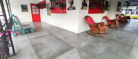 A spacious room with a high ceiling, red-framed windows, wicker rocking chairs, and a bench.
