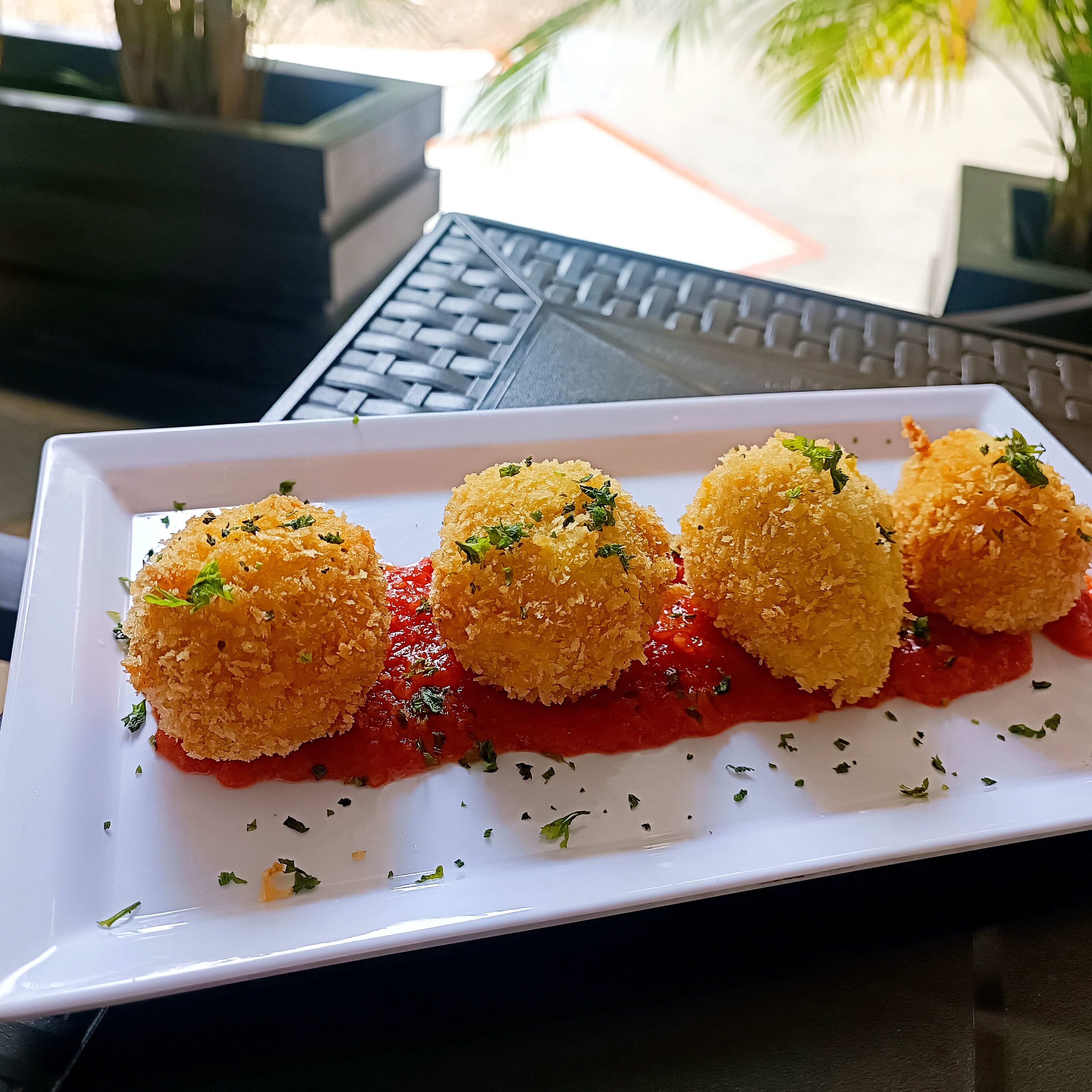 A white rectangular plate with four golden-brown fried balls garnished with herbs, served on a white surface.