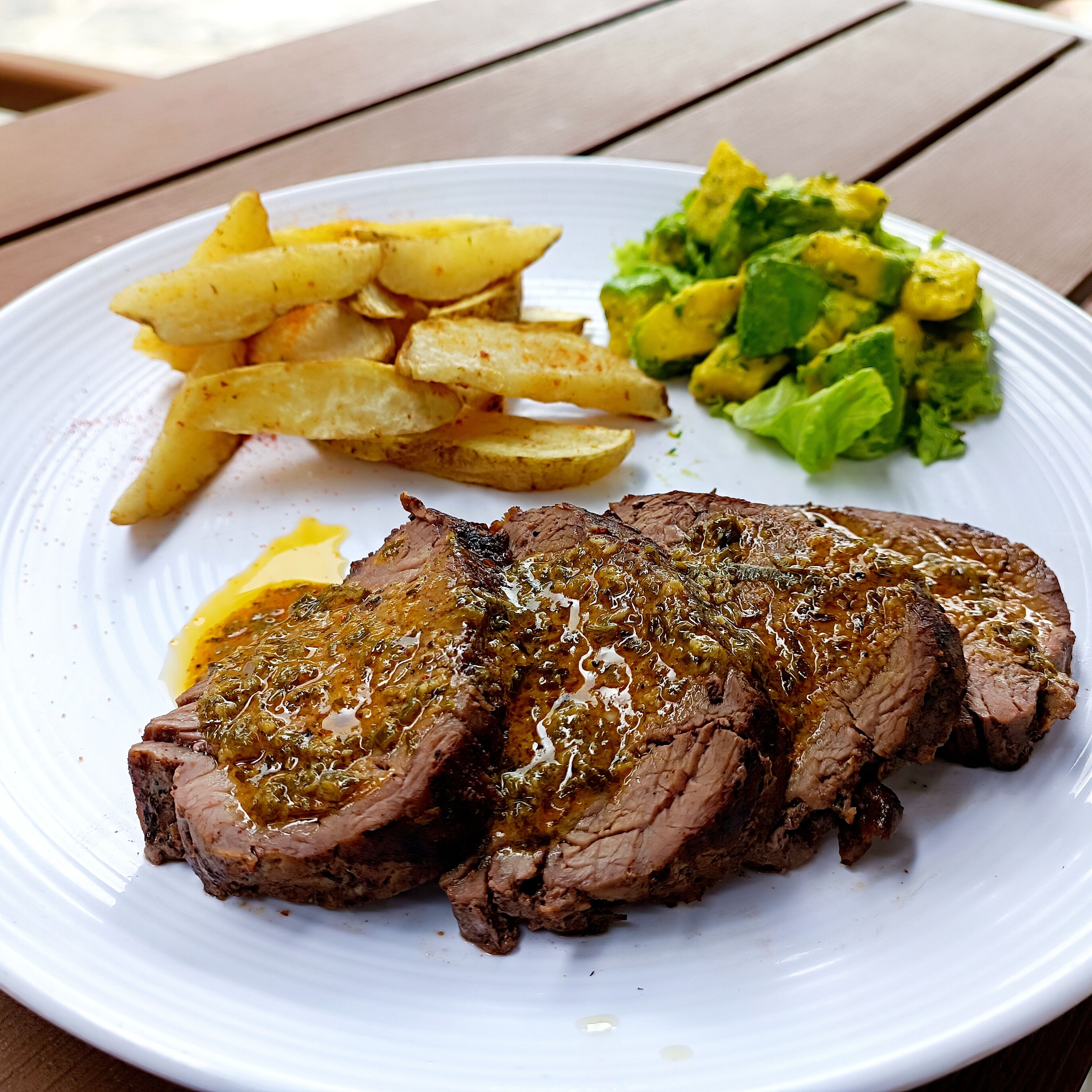 Un plato con bistec, papas fritas y una ensalada verde.