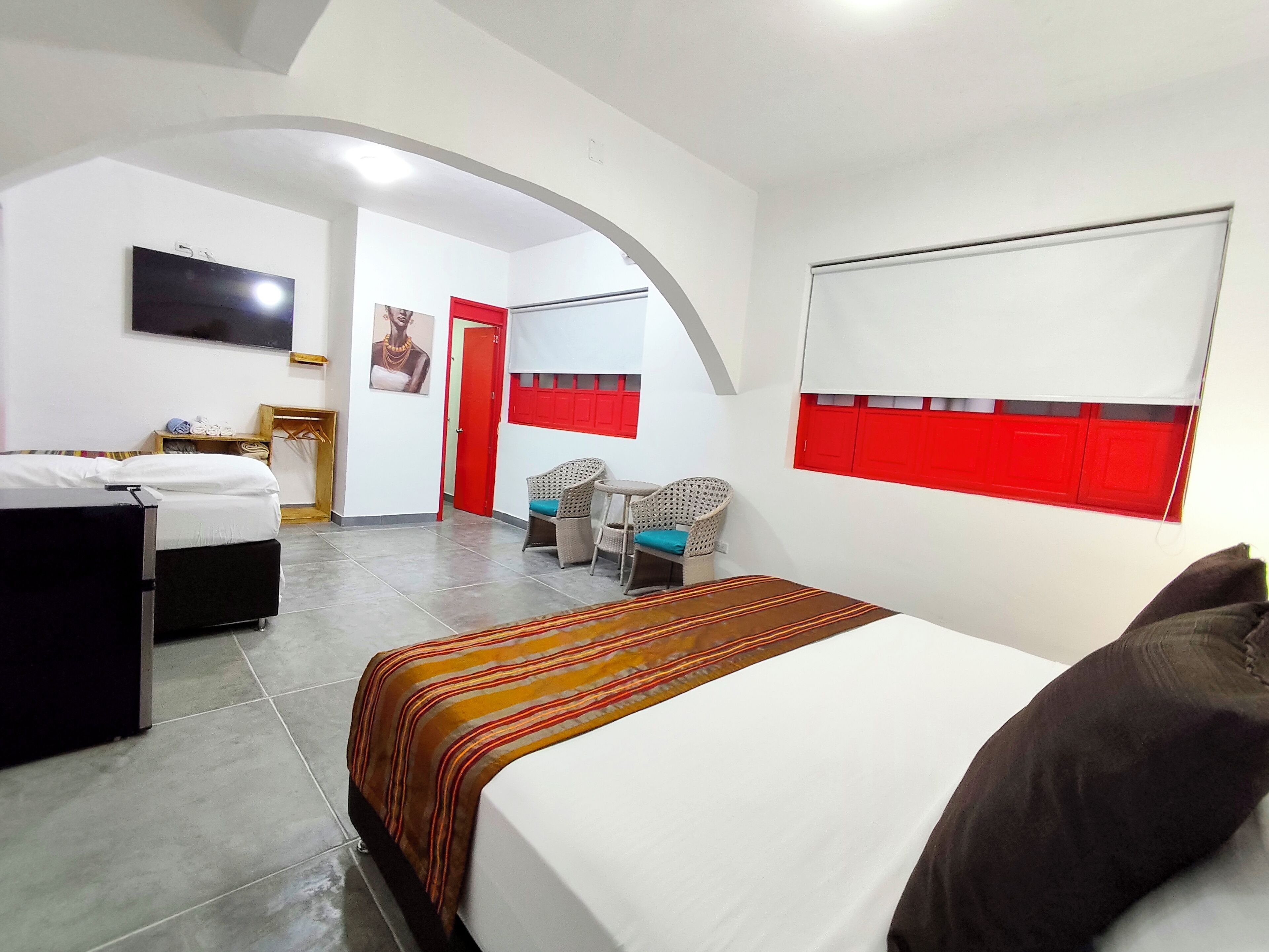 A hotel room with a bed, a TV, a chair, a small table, and a red door.