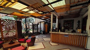 A reception area with wicker furniture, a reception desk, and a ceiling with wooden beams and a corrugated metal roof. - CASA DE PIEDRA (Melgar)