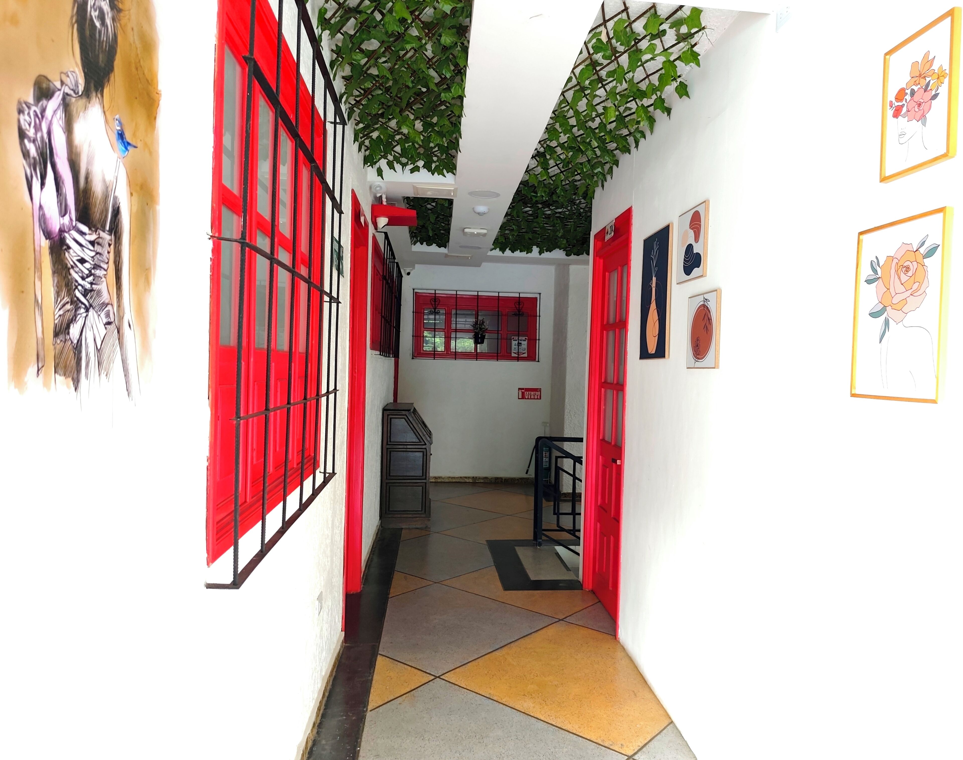 Un pasillo con ventanas de marco rojo, piso de baldosas y obras de arte colgadas en la pared.
