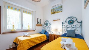 A hotel room with two beds, each with a yellow bedspread, a window with curtains, a painting on the wall, and a small bedside table with a lamp. - Villa Bluebell - Pula (Pula)