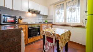 A kitchen with white cabinets, a microwave, a stove, and a table with a floral tablecloth. - Villa Bluebell - Pula (Pula)