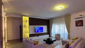 Een moderne woonkamer met een flatscreen televisie, witte banken en een salontafel.