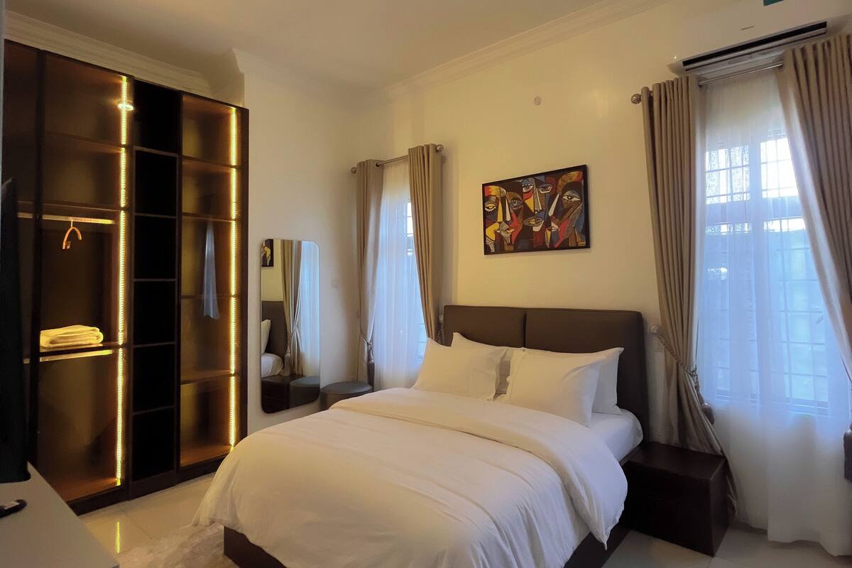Une chambre d’hôtel avec un grand lit, une armoire dotée de panneaux éclairés, un tableau au mur et une fenêtre avec des rideaux.