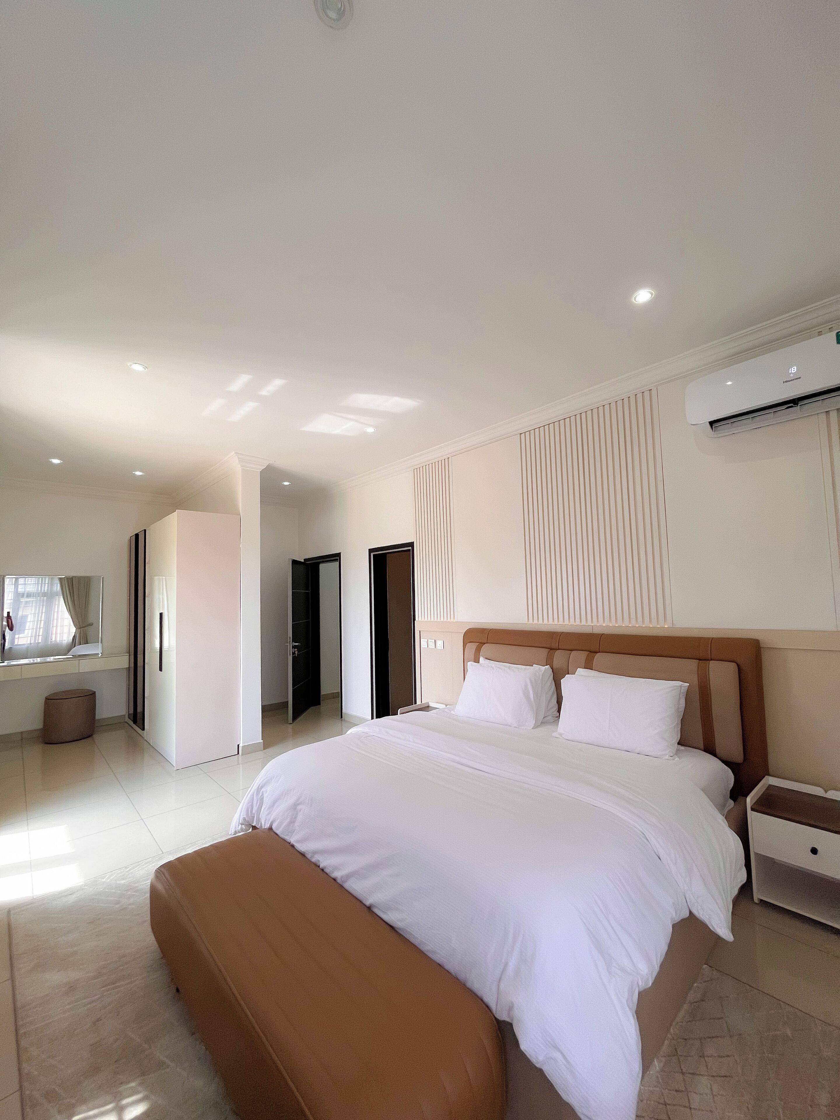 A modern bedroom with a large bed, a bedside table, and an air conditioning unit.