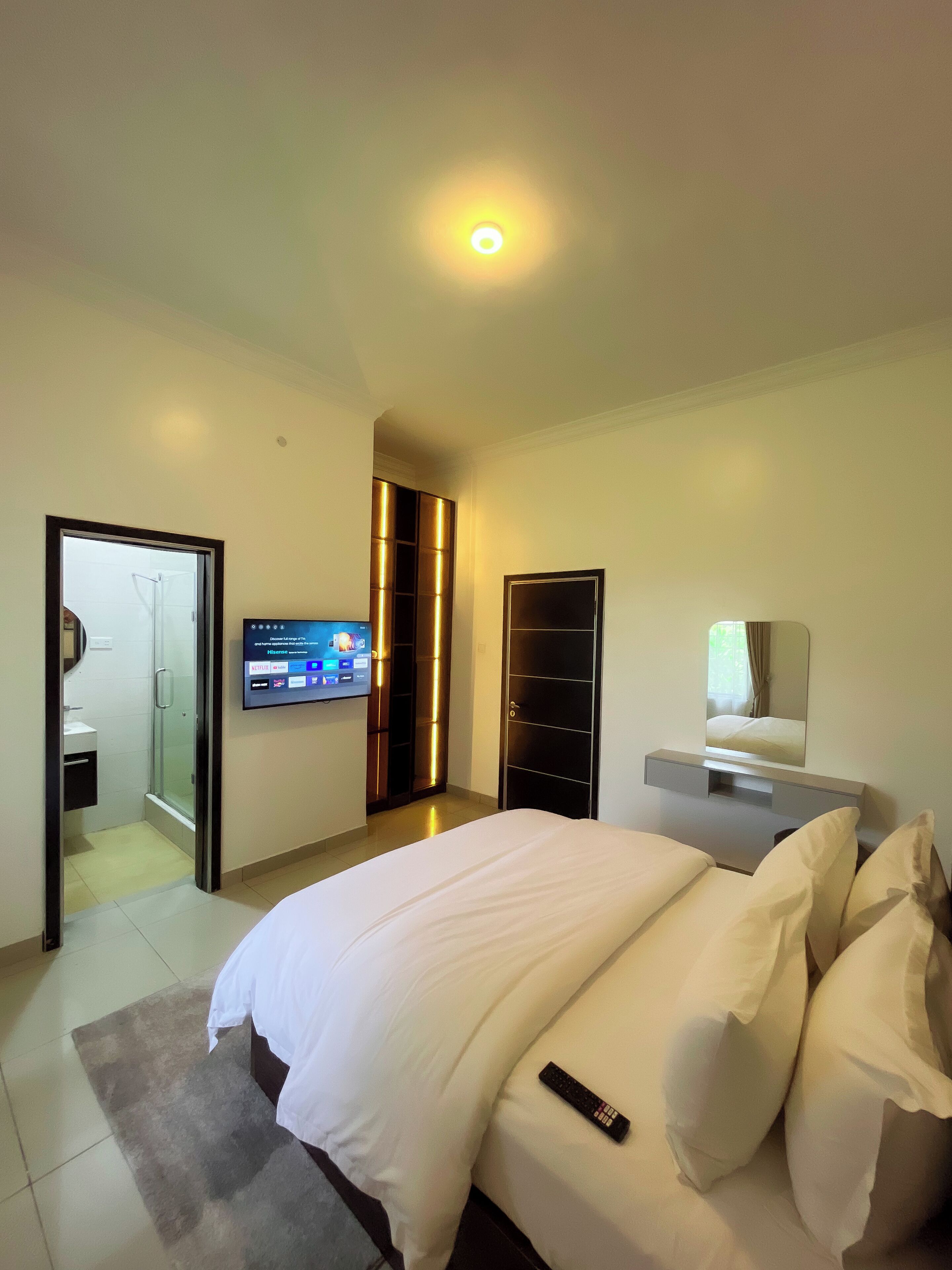 A modern hotel room with a large bed, a TV mounted on the wall, a walk-in closet, and a bathroom visible through an open door.