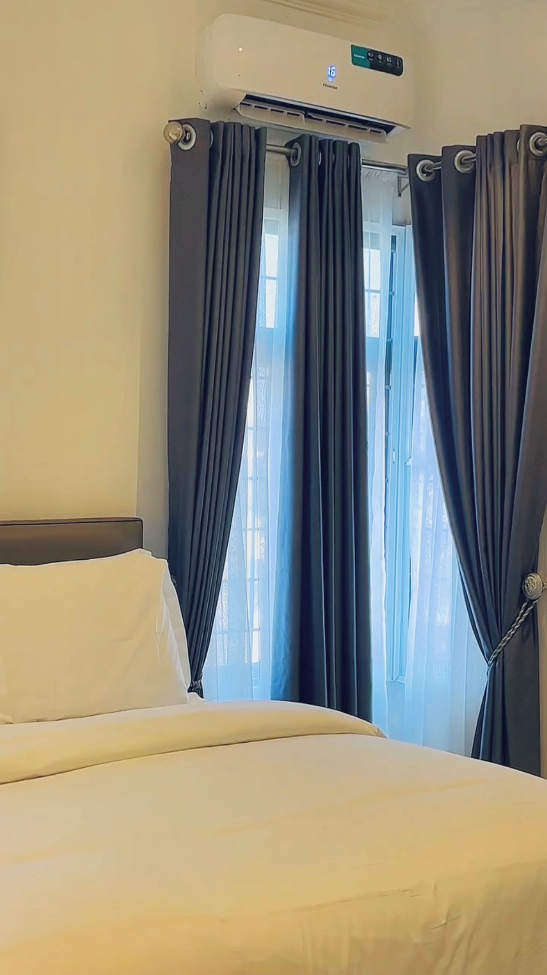 A hotel room with a bed, curtains, and an air conditioning unit.