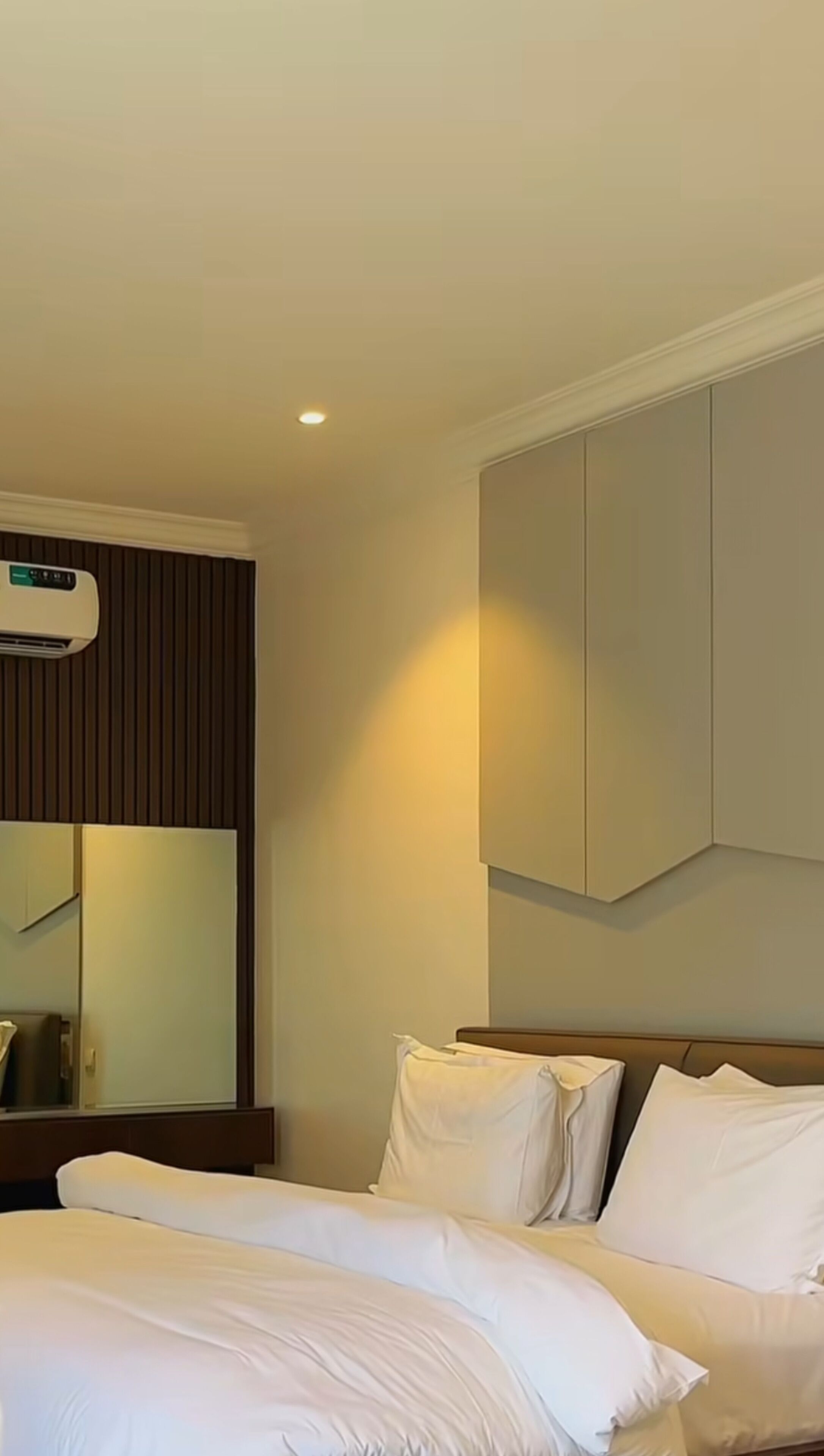 A hotel room with a bed, a large mirror, and a wall-mounted air conditioning unit.