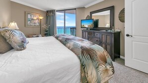 A hotel room with a bed, a television, a dresser, and a door. - Summerhouse 1012c (Panama City Beach)