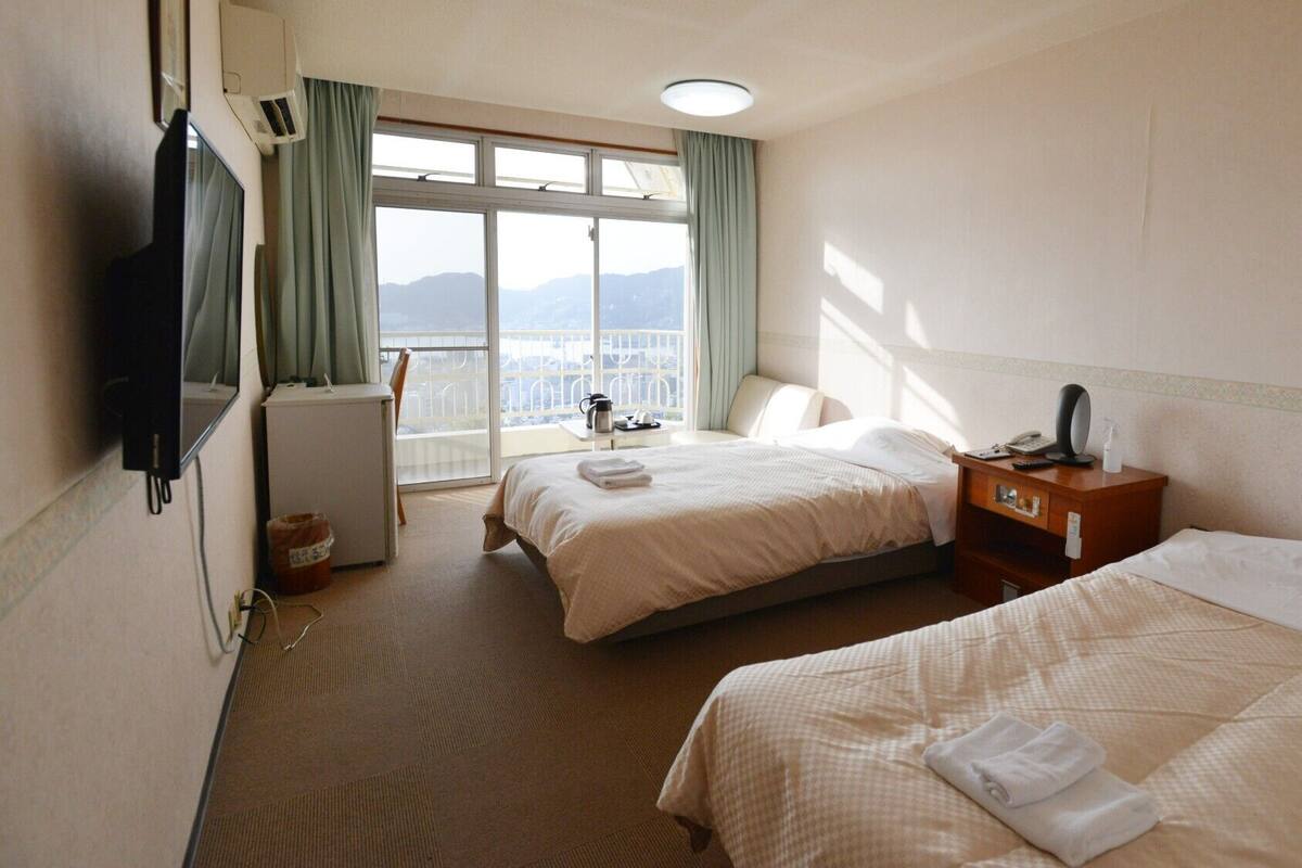A hotel room with two beds, a desk, a chair, a TV, and a window with a view.