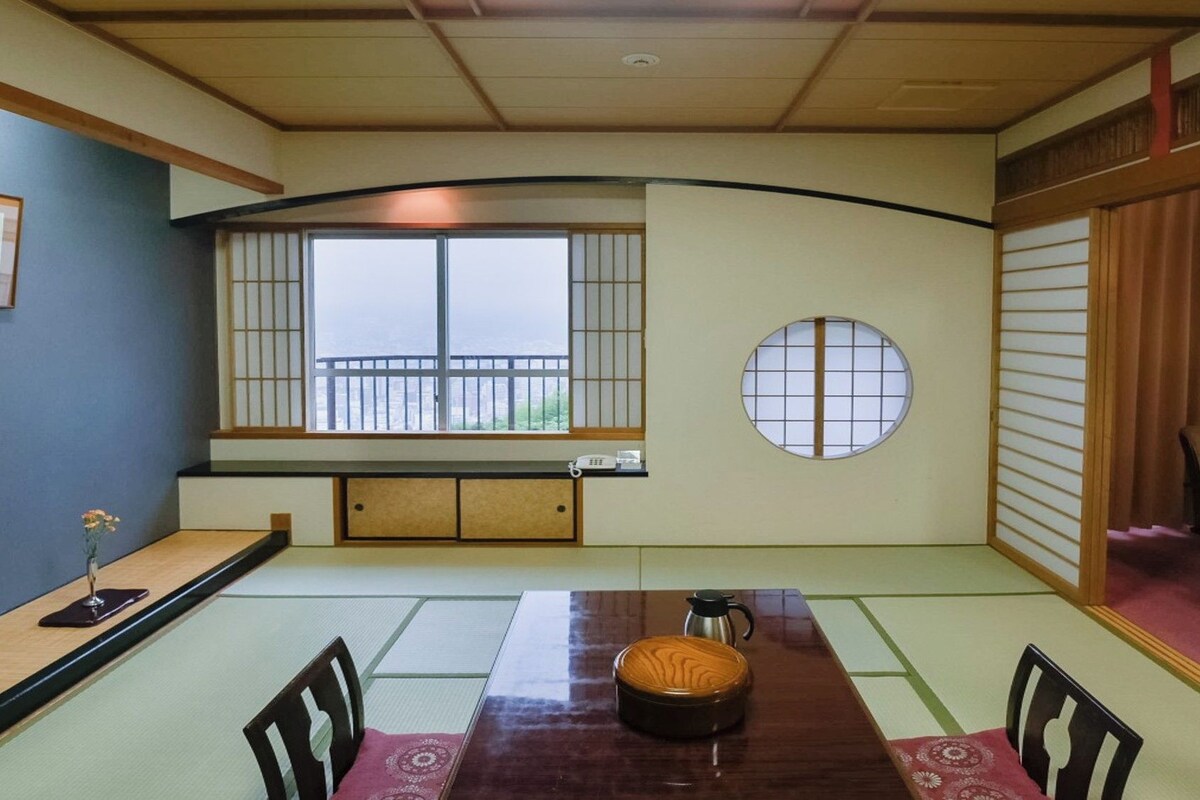 Una habitación tradicional japonesa con tatami, una mesa baja, esteras de tatami, un biombó shoji y vistas a través de la ventana.