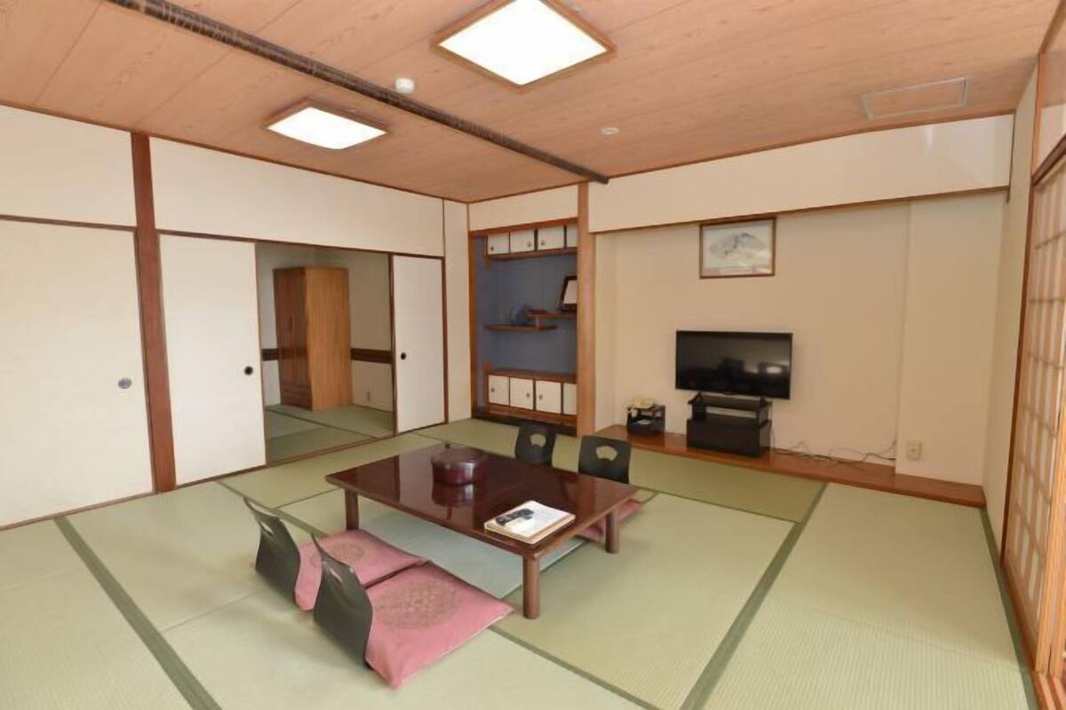 A traditional Japanese room with tatami flooring, a low table, chairs, a television, and sliding doors.