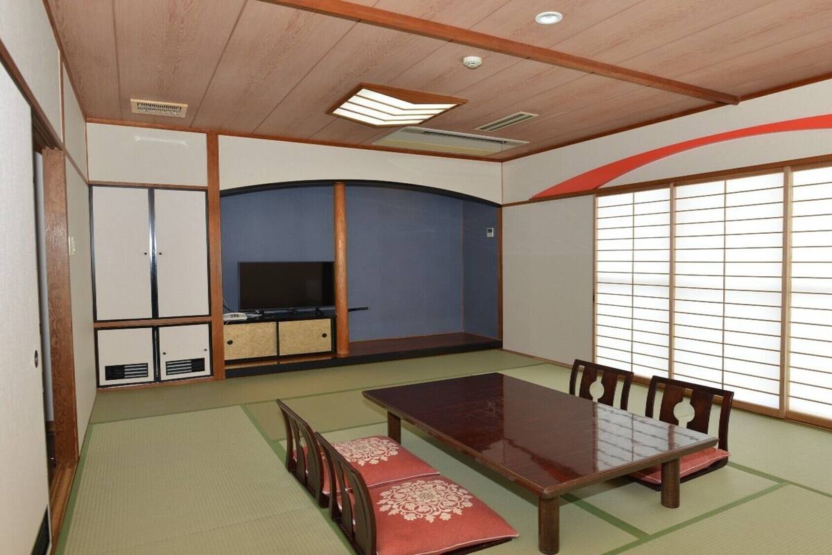 A traditional Japanese-style room with tatami flooring, a low table with chairs, a television, and sliding doors.