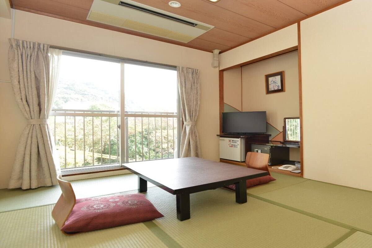 A room with tatami flooring, a low table, a television, and a small refrigerator.