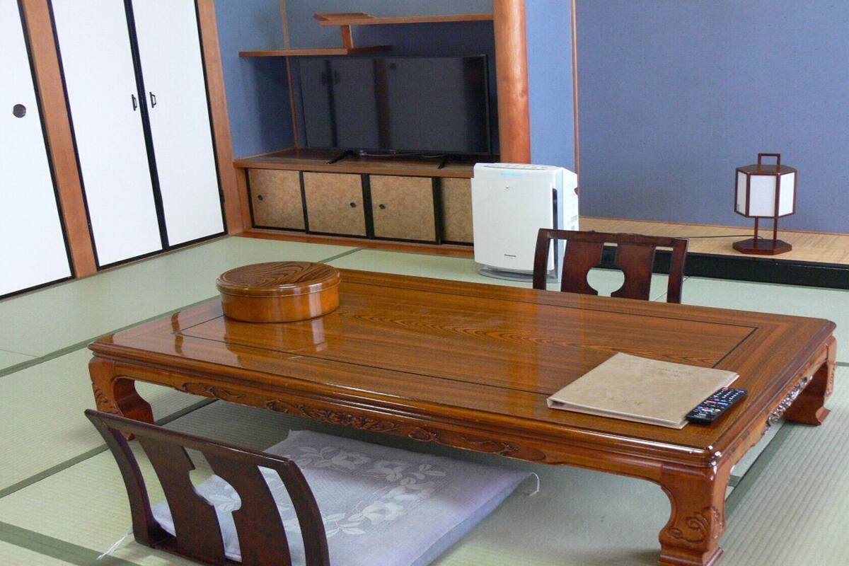 A traditional Japanese tatami room with a wooden table, chairs, a tatami mat, a refrigerator, and a lamp.