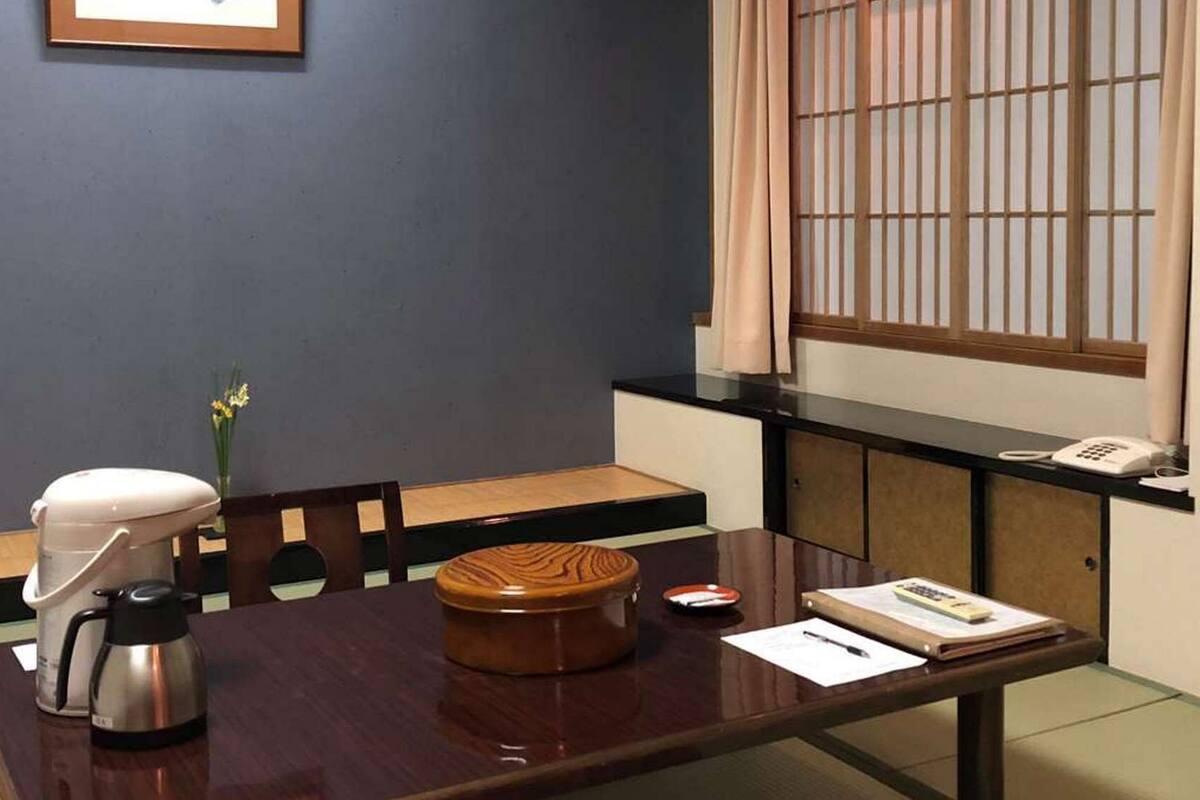 A hotel room with a wooden dining table, a coffee maker, a vase with flowers, a telephone, and a window with a view.