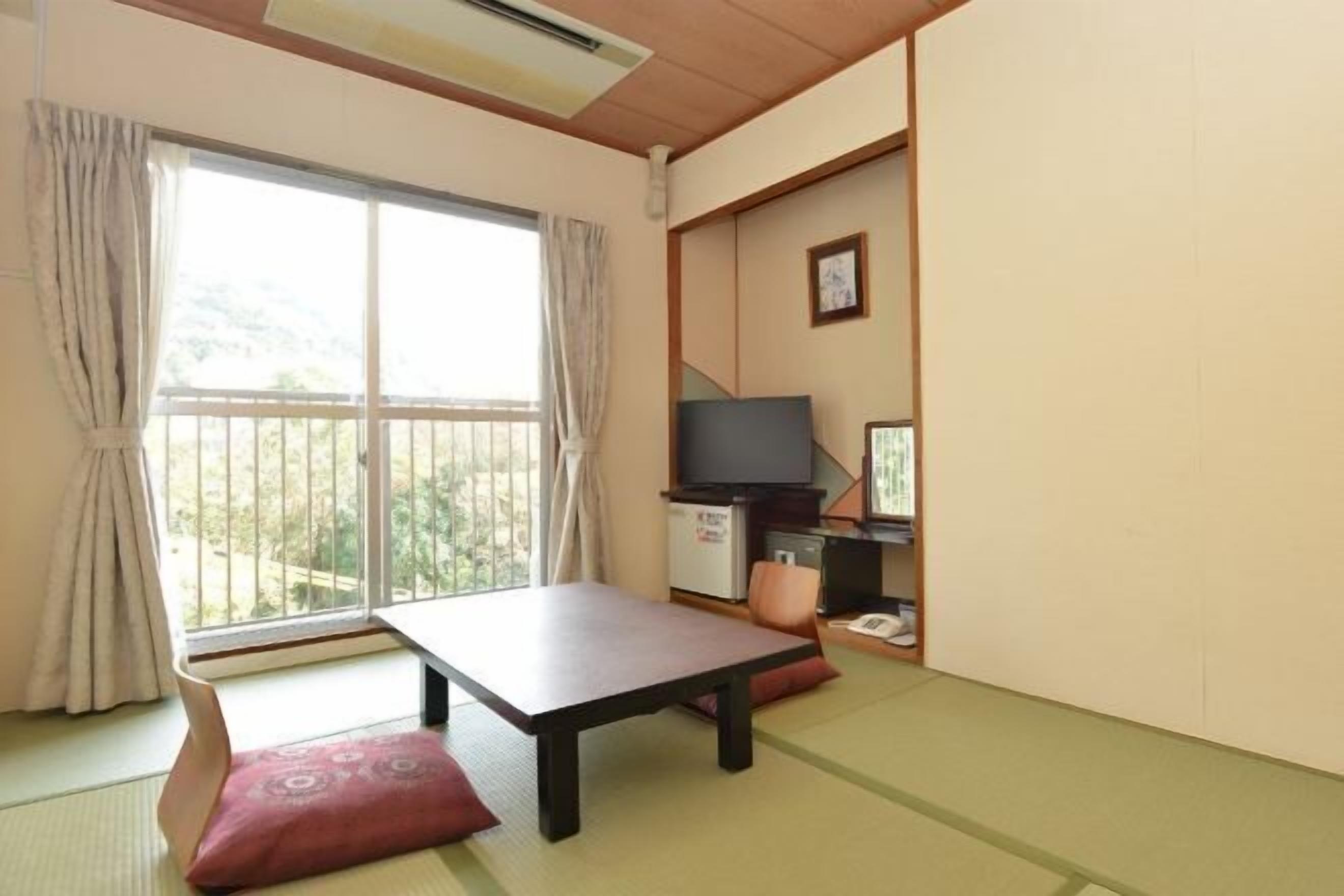A room with tatami flooring, a low table, a television, and a small kitchenette.