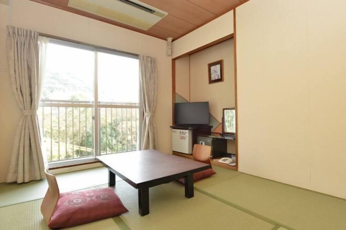 A room with tatami flooring, a low table, a television, and a small kitchenette.