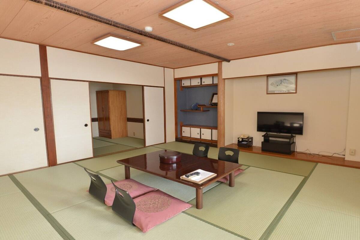 A traditional Japanese room with tatami flooring, a low table, chairs, a television, and a sliding door.
