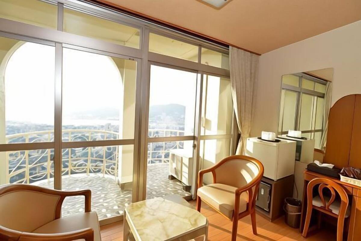A hotel room with a large balcony, a dining area with a table and chairs, and a view of the cityscape.
