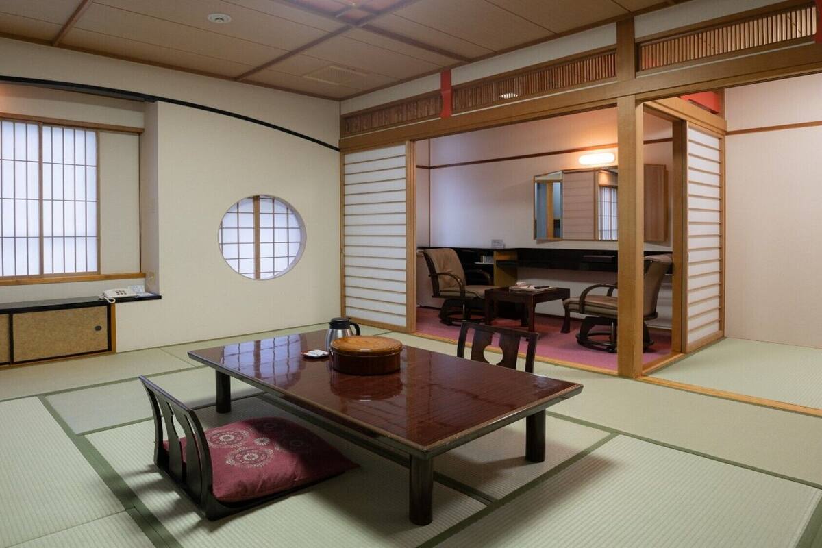 A traditional Japanese room with tatami flooring, a low table with a cushion, a round window, and sliding doors.