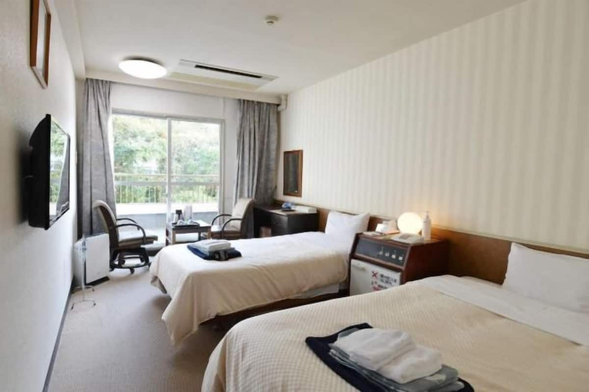A hotel room with two beds, a desk, a chair, a TV, and a window with curtains.