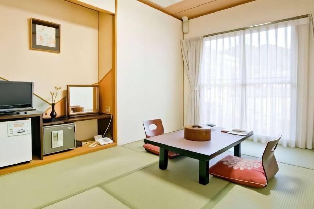 A traditional Japanese-style room with tatami flooring, a low table, a television, and a desk with a computer.
