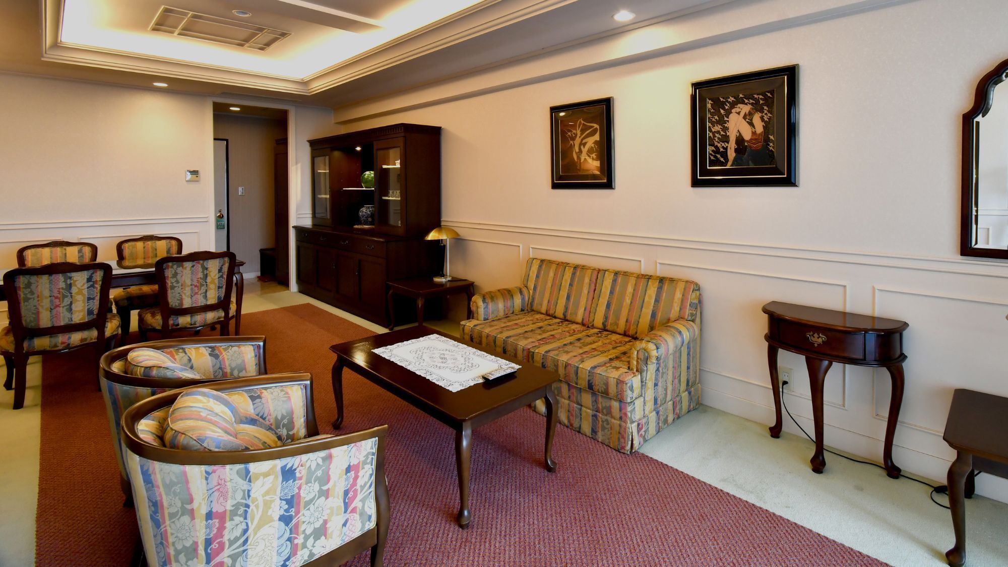 Una habitación con sofá, sillas, una mesa, un aparador y cuadros en las paredes.