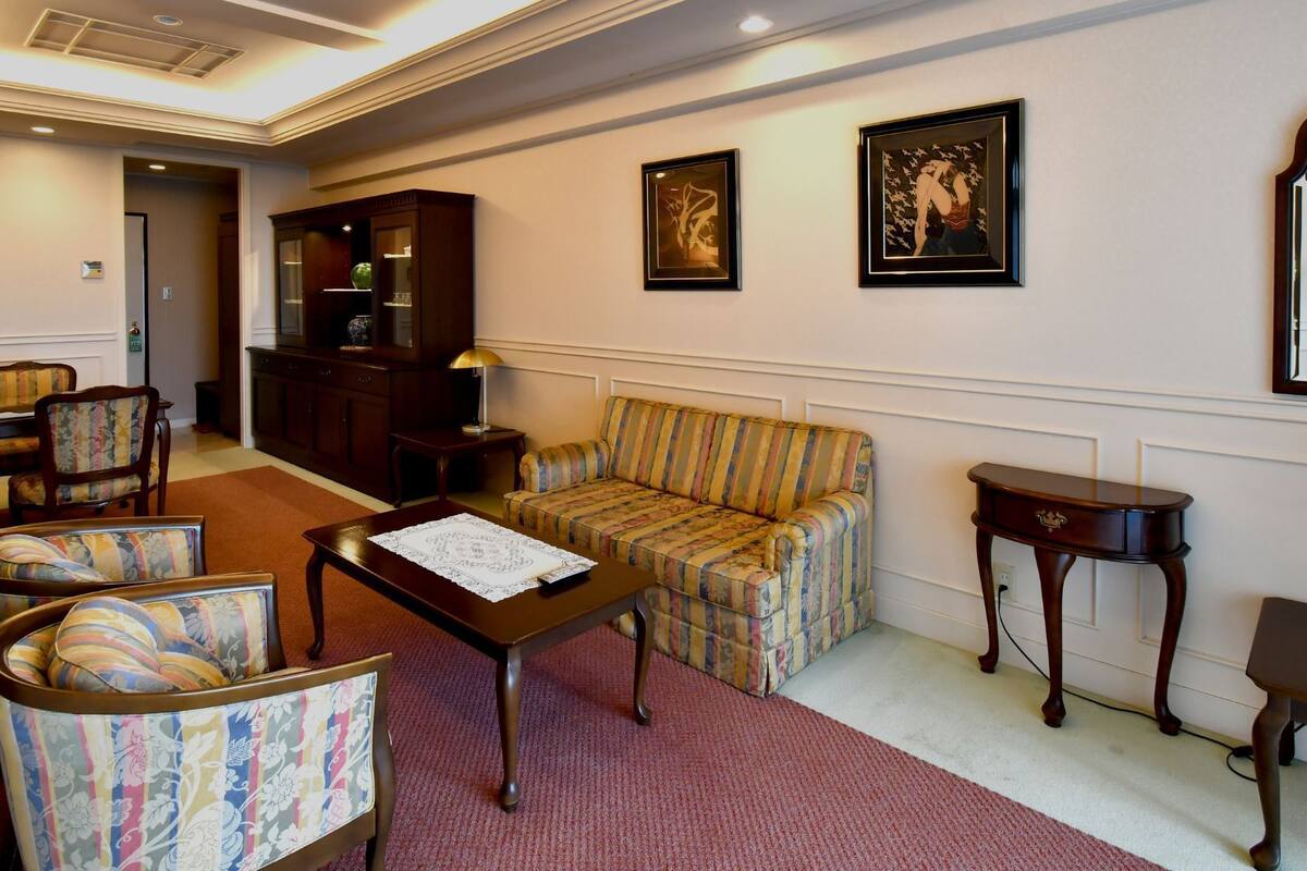 A room with a sofa, chairs, a table, a cabinet, and framed artwork on the walls.