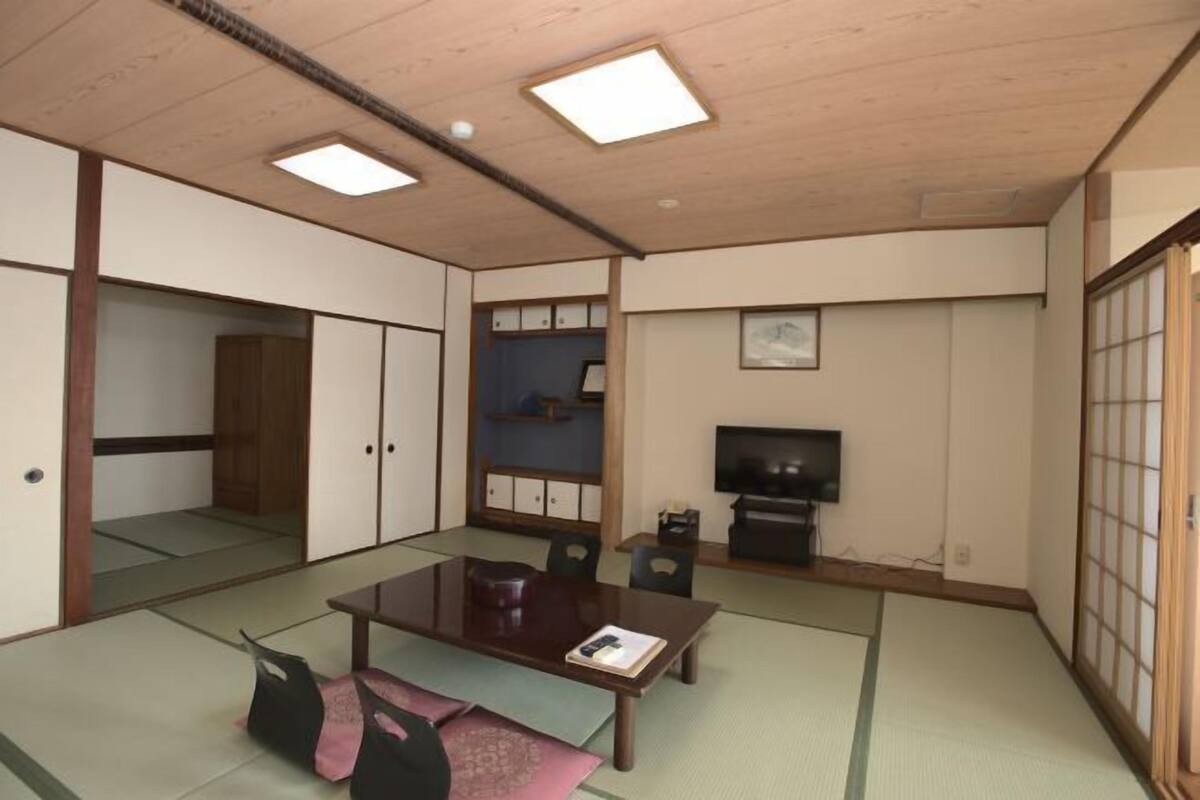 A traditional Japanese room with tatami flooring, a low table, a television, and sliding doors.